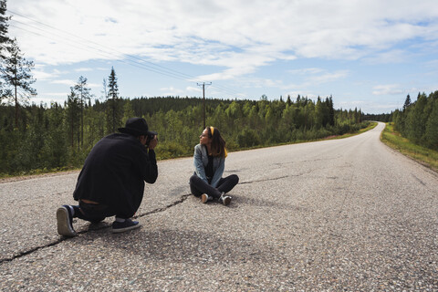 Finland, Lapland, man taking picture of woman sitting on empty country road stock photo