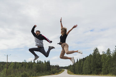 Finland, Lapland, exuberant young couple jumping in rural landscape - KKAF02083