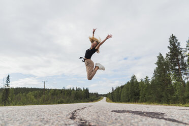 Finnland, Lappland, ausgelassene junge Frau springt in ländlicher Landschaft - KKAF02084