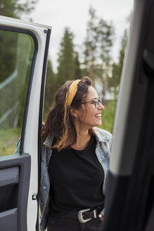 Finnland, Lappland, glückliche junge Frau an einem Auto in ländlicher Landschaft - KKAF02097