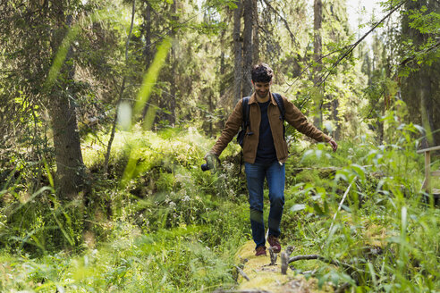 Finnland, Lappland, lächelnder Mann balanciert auf einem Baumstamm im Wald - KKAF02103