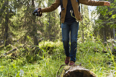 Finnland, Lappland, Mann balanciert auf Baumstamm im Wald - KKAF02104