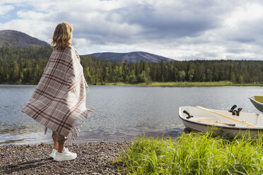 Finnland, Lappland, Frau in eine Decke gehüllt am Seeufer stehend - KKAF02109