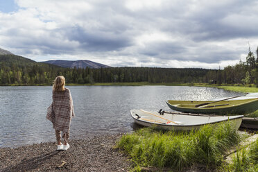 Finnland, Lappland, Frau in eine Decke gehüllt am Seeufer stehend - KKAF02111
