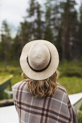 Finland, Lapland, woman wearing a hat wrapped in a blanket standing at the lakeside - KKAF02114