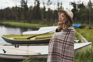 Finnland, Lappland, Frau mit Hut in eine Decke gehüllt am Seeufer stehend - KKAF02115