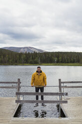 Finland, Lapland, man balancing on rod on jetty above a lake - KKAF02116