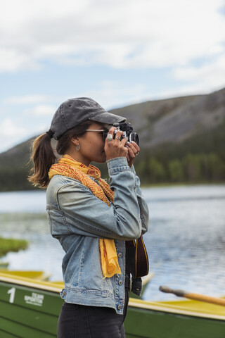Finnland, Lappland, Frau fotografiert mit einer Kamera am Seeufer, lizenzfreies Stockfoto