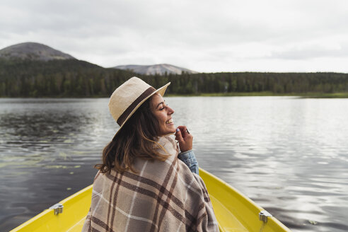 Finland, Lapland, happy woman wearing a hat on a boat on a lake - KKAF02123