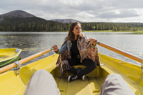 Finland, Lapland, woman wearing a blanket in a rowing boat on a lake - KKAF02128