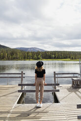 Finnland, Lappland, Frau mit Hut steht auf einem Steg an einem See - KKAF02133