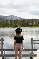 Finnland, Lappland, Frau mit Hut steht auf einem Steg an einem See - KKAF02134