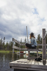 Finnland, Lappland, entspannte Frau sitzt auf einem Steg an einem See - KKAF02143