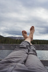 Mann sitzt auf einem Steg an einem See und hält seine Füße hoch - KKAF02144