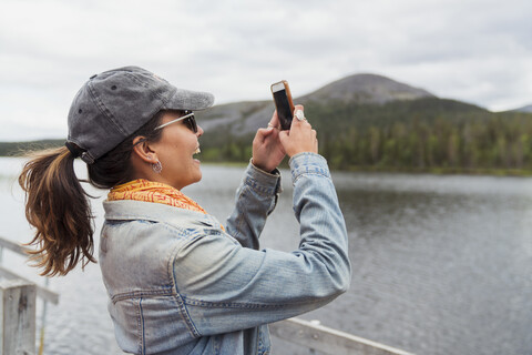 Finnland, Lappland, glückliche Frau auf Steg an einem See, die ein Selfie macht, lizenzfreies Stockfoto