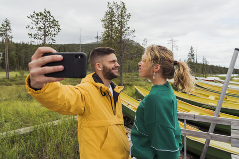 Finnland, Lappland, junges Paar macht ein lustiges Selfie am Seeufer, lizenzfreies Stockfoto