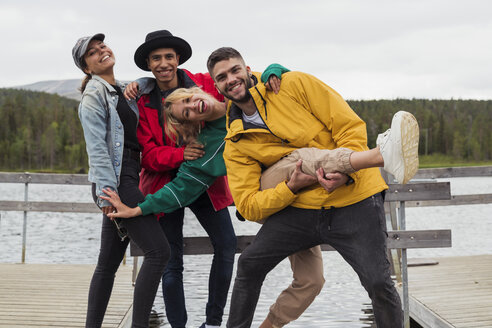 Finland, Lapland, portrait of happy playful friends on jetty at a lake - KKAF02155