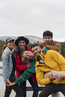 Finland, Lapland, portrait of happy playful friends on jetty at a lake - KKAF02156