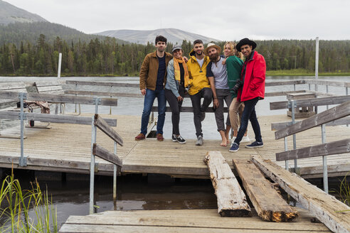 Finland, Lapland, portrait of friends standing on jetty at a lake - KKAF02158