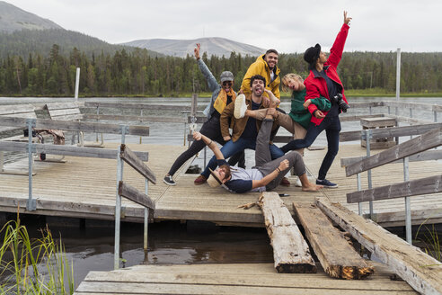 Finland, Lapland, portrait of happy playful friends posing on jetty at a lake - KKAF02159