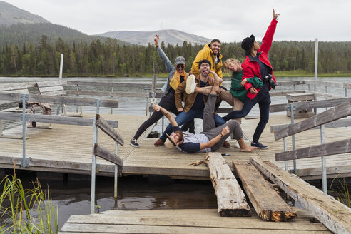 Finnland, Lappland, Porträt von fröhlichen, verspielten Freunden, die auf einem Steg an einem See posieren - KKAF02159