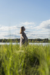 Finland, Lapland, woman wrapped in a blanket standing at the lakeside - KKAF02164