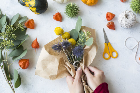 Autumnal decoration, ornamental pumpkins, hands wrapping bunch of flowers - JUNF01328