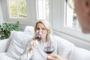 Porträt einer blonden reifen Frau, die mit ihrem Partner zu Hause Rotwein trinkt - FMKF05313