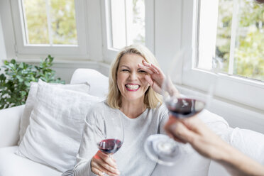 Porträt einer lachenden blonden reifen Frau, die zu Hause mit Rotwein anstößt - FMKF05314