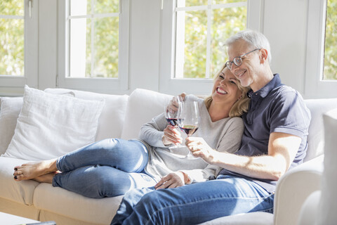 Reifes Paar entspannt sich auf der Couch mit Rotwein und hat Spaß, lizenzfreies Stockfoto