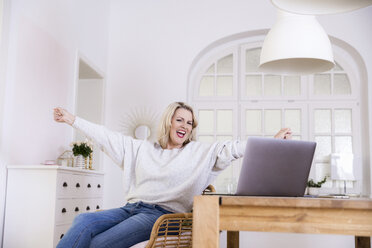 Porträt einer glücklichen blonden reifen Frau mit Laptop zu Hause - FMKF05326
