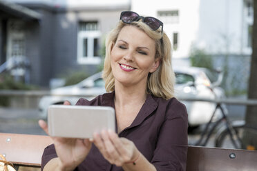Porträt einer lächelnden blonden reifen Frau, die im Freien ein Smartphone benutzt - FMKF05332