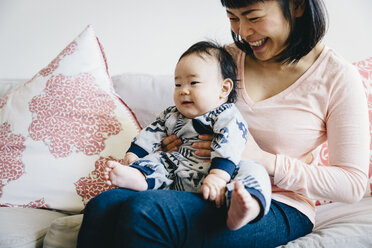 Happy mother with cute son sitting on sofa in living room - CAVF48963