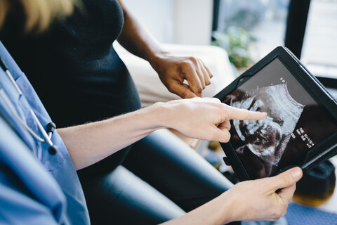 Mittelteil eines Arztes, der einer schwangeren Frau im Krankenhaus sitzend auf einem Tablet-Computer eine Ultraschalluntersuchung zeigt, lizenzfreies Stockfoto