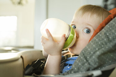 Porträt eines kleinen Jungen, der Milch trinkt, während er zu Hause auf einem Hochstuhl sitzt - CAVF48984