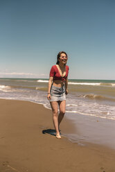 Glückliche Frau, die am Strand gegen den blauen Himmel an einem sonnigen Tag spazieren geht - CAVF48985
