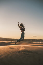 Glückliche Frau springt am Strand gegen den Himmel bei Sonnenuntergang - CAVF48988