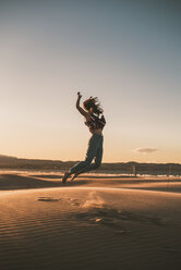 Happy woman jumping at beach against sky during sunset - CAVF48988