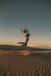 Glückliche Frau springt am Strand gegen blauen Himmel bei Sonnenuntergang - CAVF48989