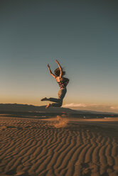 Happy woman jumping at beach against blue sky during sunset - CAVF48989