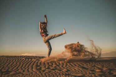 Happy woman playing with sand at beach against blue sky during sunset - CAVF48990