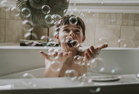 Happy boy playing with bubbles while taking bath in bathtub stock photo