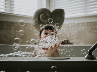 Boy playing with bubbles while taking bath in bathtub - CAVF48996