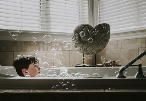 Junge schaut sich die Blasen an, während er ein Bad in der Badewanne nimmt, lizenzfreies Stockfoto