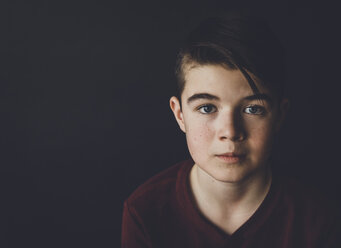 Portrait of confident boy standing against black background - CAVF49000