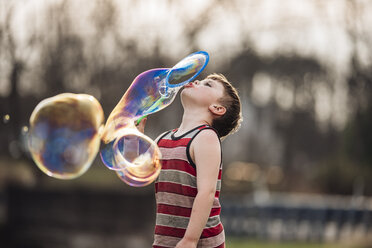 Junge bläst Seifenblasen beim Spielen im Park - CAVF49002
