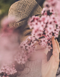 Nahaufnahme einer jungen Frau mit Kirschblüten und Hut im Park - CAVF49003