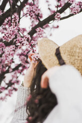 Nahaufnahme einer jungen Frau, die Kirschblüten auf einem Zweig im Park hält - CAVF49006