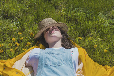 High angle view of carefree young woman with hat lying on grassy field at park - CAVF49015