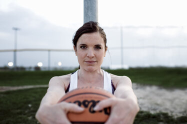 Portrait of woman holding basketball while standing by pole against sky during sunset - CAVF49031